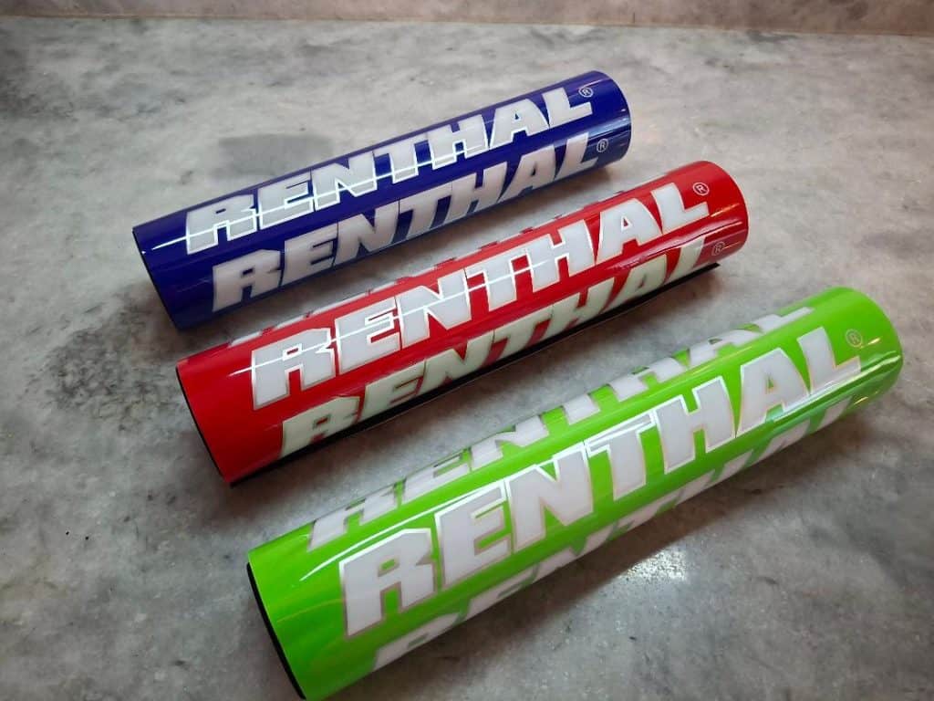 Three colorful Renthal fuel containers in blue, red, and green on a concrete surface.
